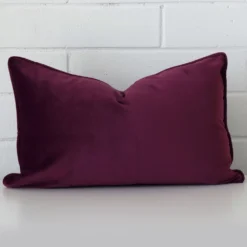 An attractive velvet cushion in front of a white brick wall. It has a rectangle shape and is purple in colour.