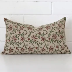 Sesigner rectangle cushion with a floral design in an upright position against a white brick wall.