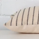 Striped cushion cover laying sideways against brick wall. The rectangle size and designer material are shown highlighting the seams.