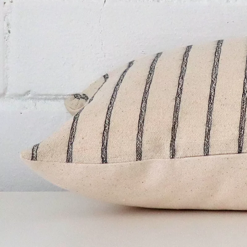 Striped cushion cover laying sideways against brick wall. The rectangle size and designer material are shown highlighting the seams.