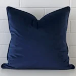 Royal blue Tcushion cover in front of a white wall. It has a large size and is made from a velvet material.