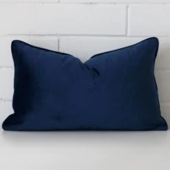 Royal blue cushion cover sits against a white wall. It is constructed from a superior looking velvet material and has rectangle dimensions