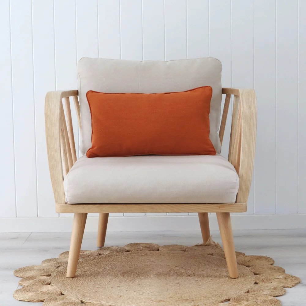 A rust cushion sits in the middle of a wood coloured chair.