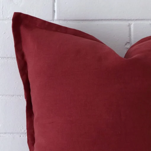 The corner of this rust linen cushion is shown close up. The finer detail of its square design can be seen.