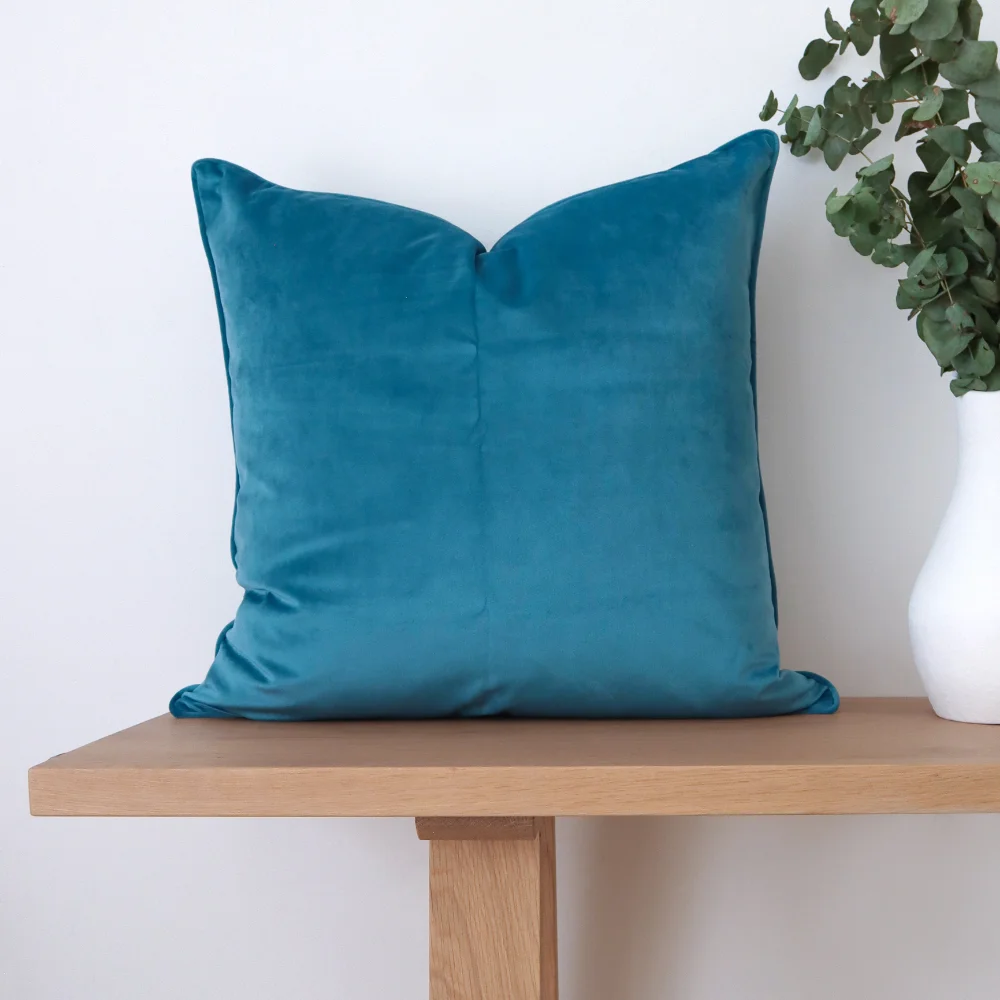 A teal cushion displayed on a light coloured bench.