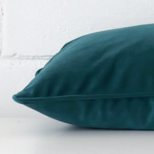 A sideways perspective of this velvet cushion. The positioning shows the border of the rectangle shape and the teal colour.