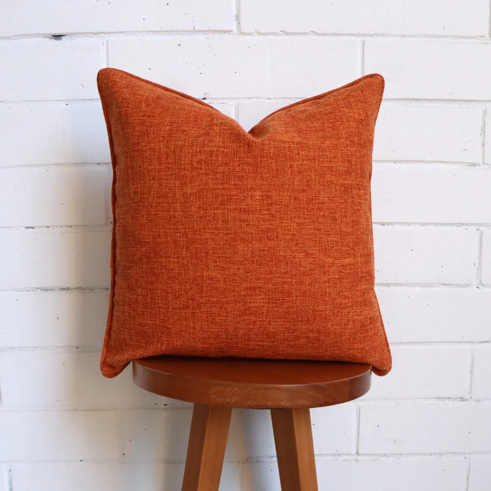 A terracotta cushion positioned vertically on a dark timber stool.