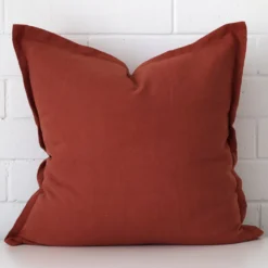 Terracotta cushion cover in front of a white wall. It has a square size and is made from a linen material.