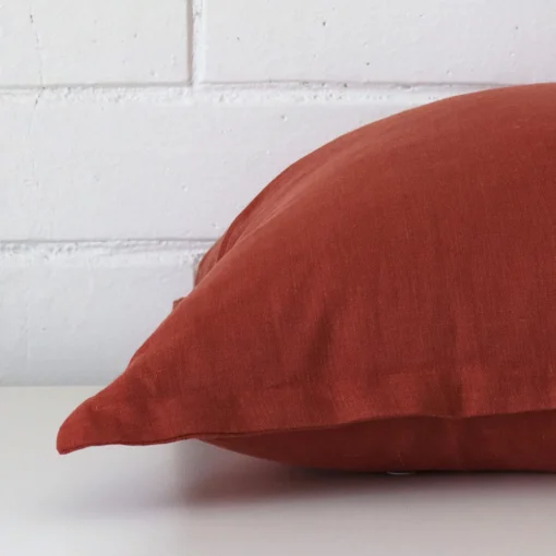 Lateral view of front and back panels of this linen cushion cover in a square size and with terracotta colouring.