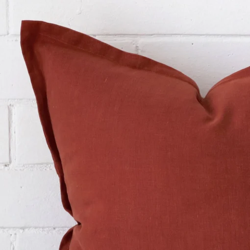 The corner of this linen square cushion cover is shown close up. The terracotta colour is shown in greater detail.