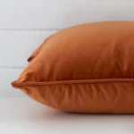 A sideways perspective of this velvet cushion. The positioning shows the border of the large shape and the terracotta colour.