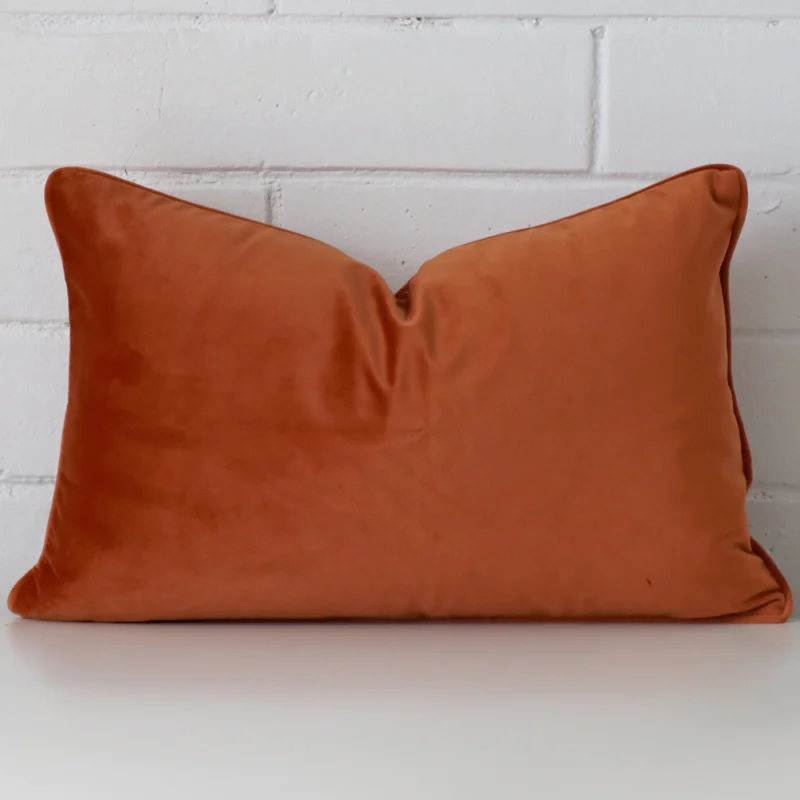 terracotta-velvet-rectangular-cushion-cover-30cm-x-50cm-sc770-30 Velvet rectangle cushion in an upright position against a white brick wall. It is terracotta in colour.