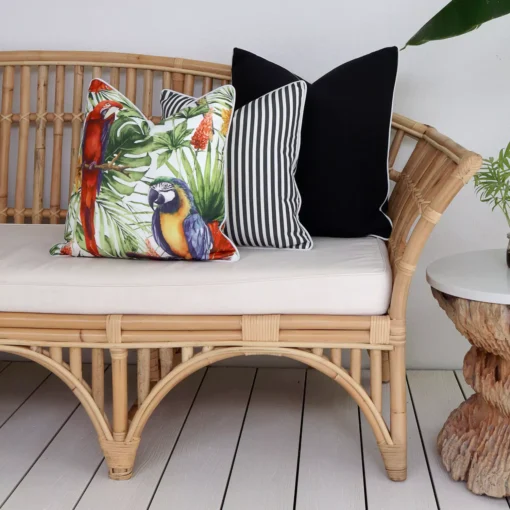 A rattan seat adorned with a set of 3 tropical black outdoor couch cushions.