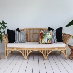 Five tropical black outdoor cushions arranged on a rattan seat in a breezy lounge.