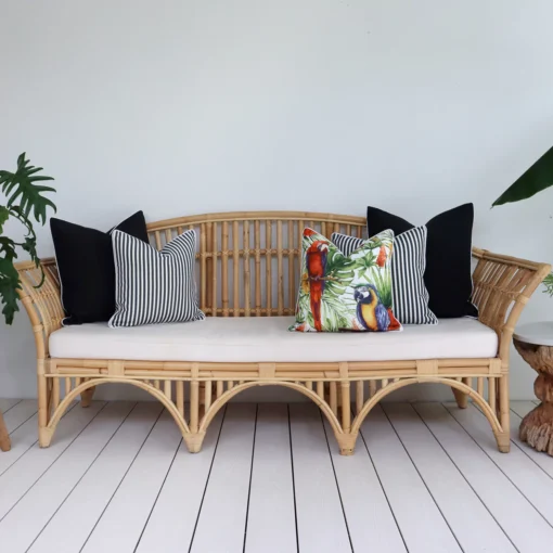 Five tropical black outdoor cushions arranged on a rattan seat in a breezy lounge.