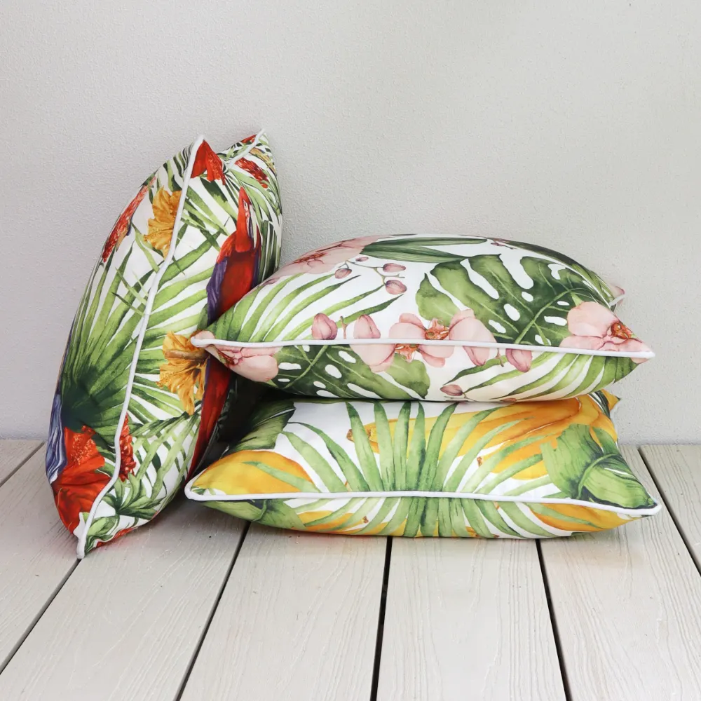 Three tropical outdoor cushions stacked outside on a wooden floor.