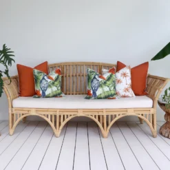 A rattan seat positioned between two leafy plants with a set of five tropical terracotta outdoor cushions.