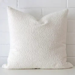 White cushion cover in front of a white wall. It has a square size and is made from a boucle material.