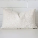 White cushion cover sits against a white wall. It is constructed from a superior looking boucle material and has rectangle dimensions.