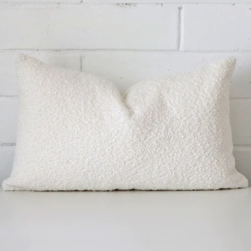 White cushion cover sits against a white wall. It is constructed from a superior looking boucle material and has rectangle dimensions.