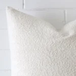 Close up view showing a corner of this boucle cushion in a rectangle size and with white colouring.