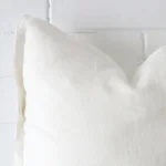 Square cushion in white colour sitting upright in front of a brick wall. It has been made from a quality linen material.