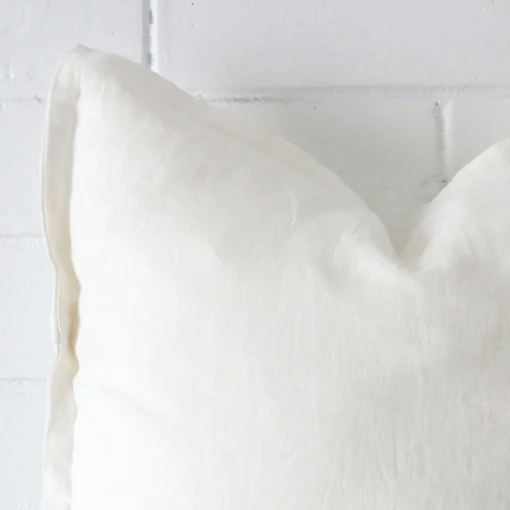 Square cushion in white colour sitting upright in front of a brick wall. It has been made from a quality linen material.