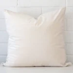 White wall with a white cushion laying against it. It has a distinctive velvet fabric and has a large size.