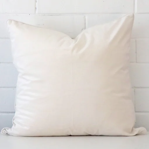 White wall with a white cushion laying against it. It has a distinctive velvet fabric and has a large size.