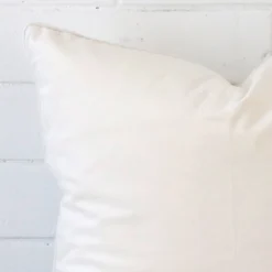 Close range image of white cushion. The square size and velvet material can be seen in detail.