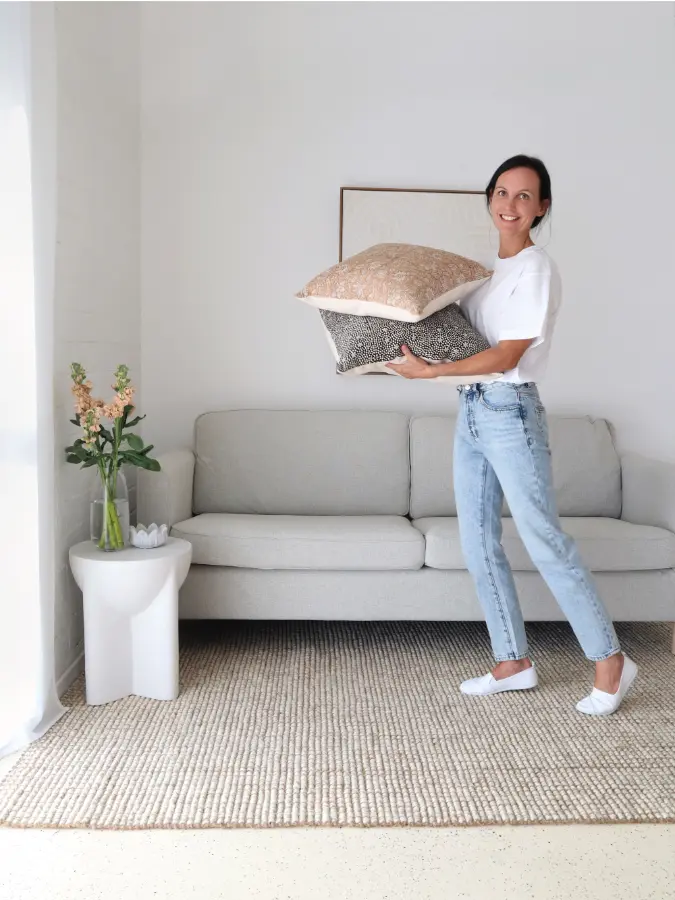 A woman is holding two cushions in her arms in a living room.