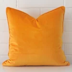 Large cushion cover in yellow colour sitting upright in front of a brick wall. It has been made from a quality velvet material.