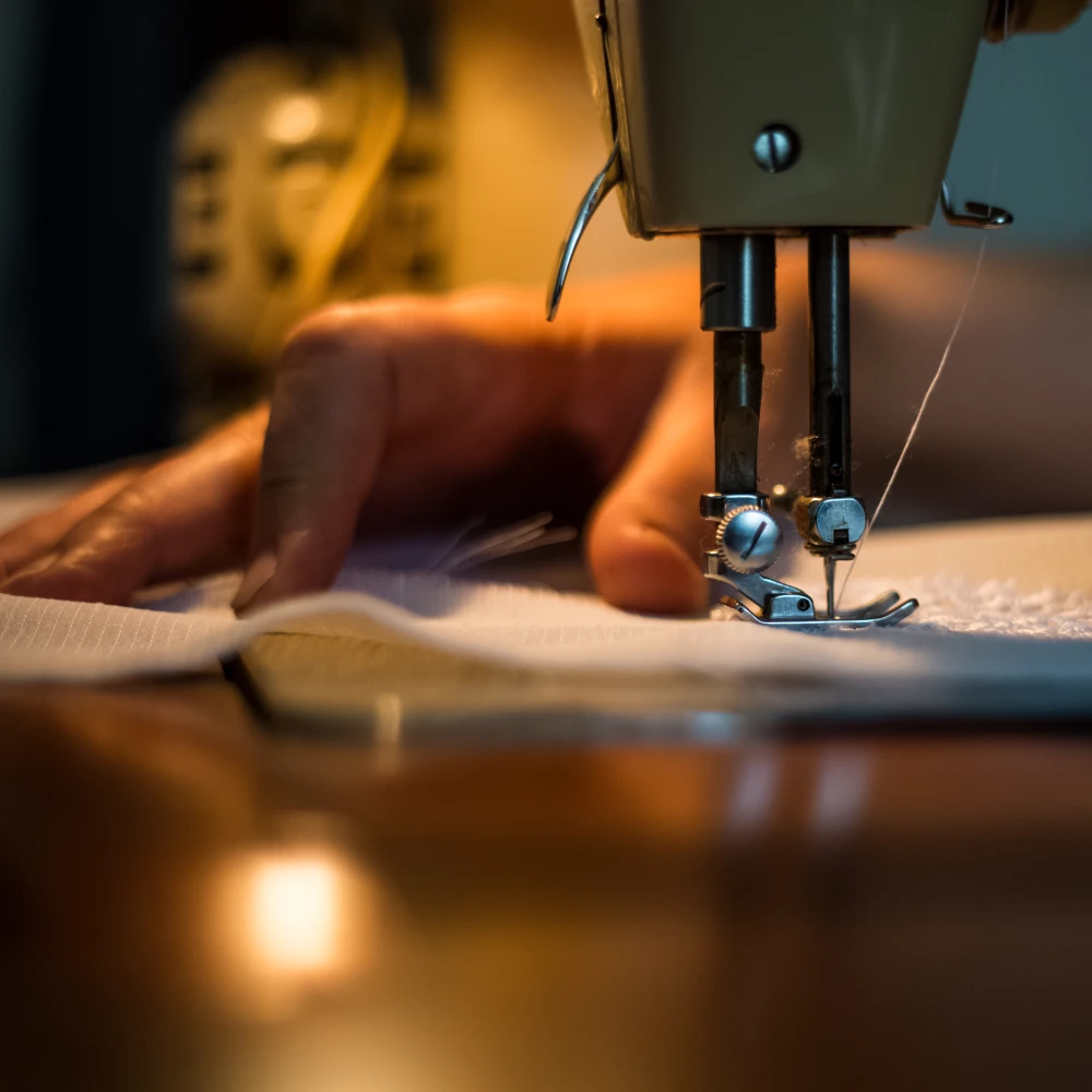 Hands are using a sewing machine under a dim light.