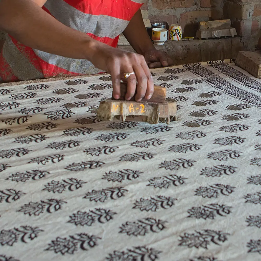 A man is creating an Indian block printed piece of fabric using a stamp.