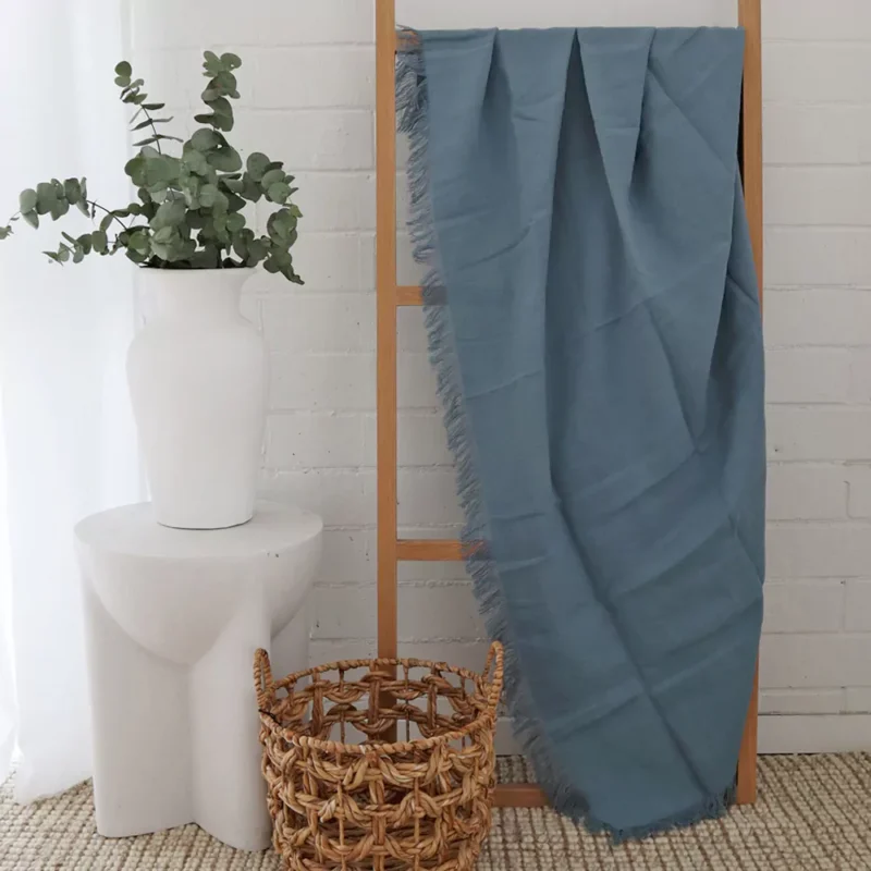 Blue Linen Throw -TH813 A stylish wooden rack in a white room with a blue linen throw hanging on it.