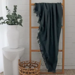 A green linen throw hanging on a wooden rack in a white room.