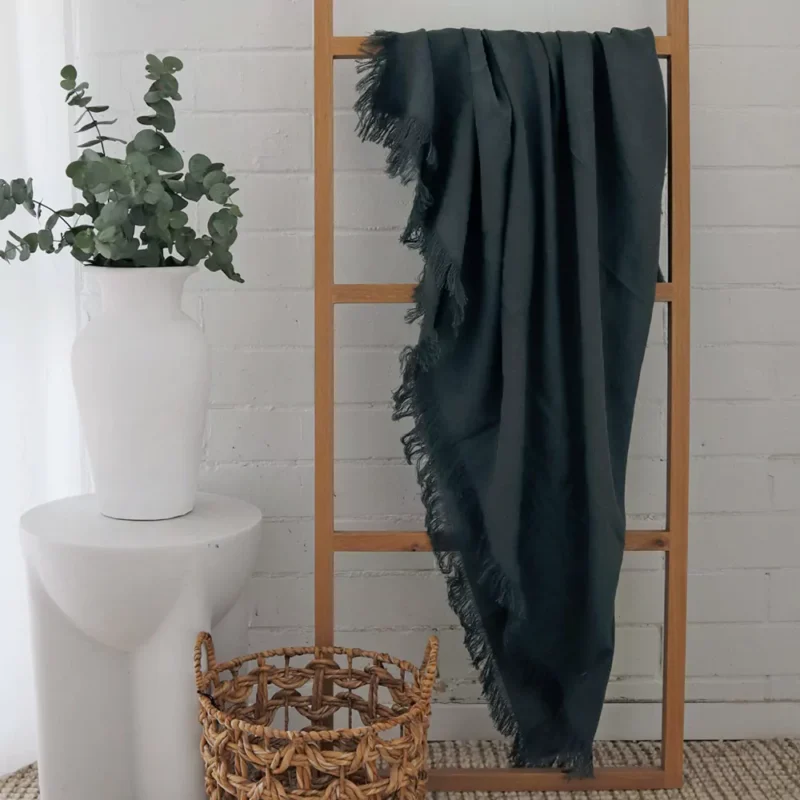 Green Linen Throw - TH811 A green linen throw hanging on a wooden rack in a white room.