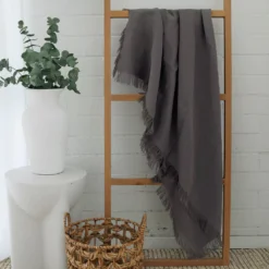 A wooden rack against a white wall styled with a grey linen throw.