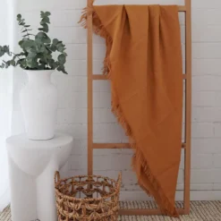 A mustard linen throw hanging on a wooden rack standing in front of a white brick wall.