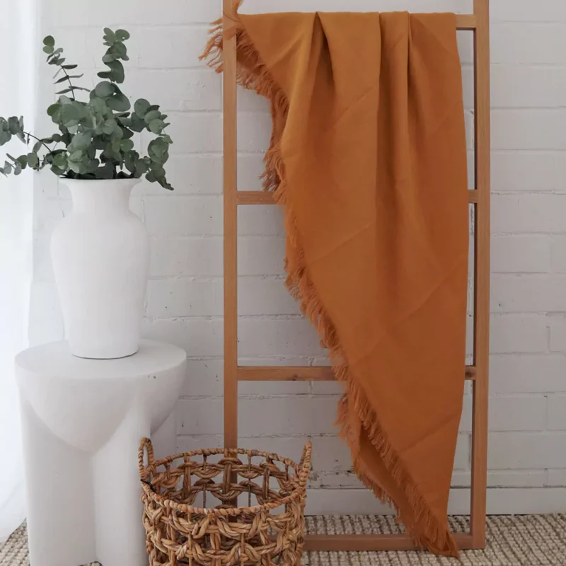 Mustard Linen Throw - TH818 A mustard linen throw hanging on a wooden rack standing in front of a white brick wall.