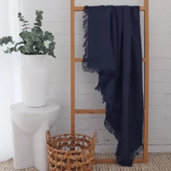 A navy linen throw displayed in a white room with a wooden rack.