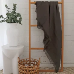 A white room with an olive-coloured linen throw hanging on a wooden rack.