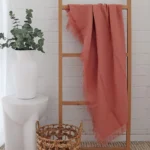 A rack in front of a white brick wall with a pink linen throw hanging on it.