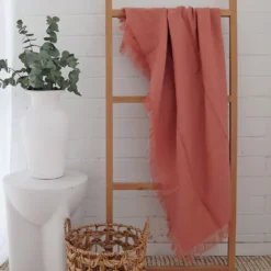 A rack in front of a white brick wall with a pink linen throw hanging on it.