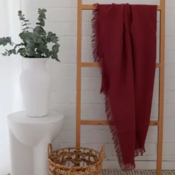 A rust-coloured linen throw hanging on a rack in a white room.