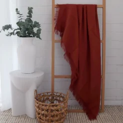 A terracotta linen throw is displayed on a wooden rack in a white room.