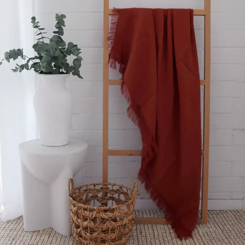 Terracotta Linen Throw - TH817 A terracotta linen throw is displayed on a wooden rack in a white room.