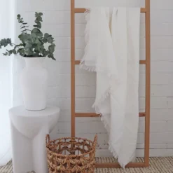 A wooden rack with a white linen throw hanging on it.