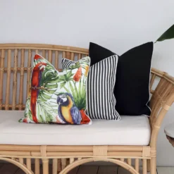 3 outdoor cushions in a tropical design and black colour are shown on a couch.
