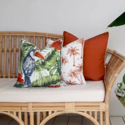 A couch with 3 vibrant terracotta-coloured couch cushions in a tropical style.